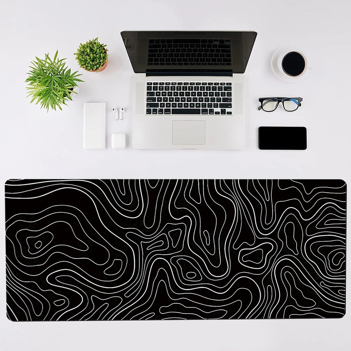 A black desk setup featuring a laptop, mouse, keyboard, and a large black and white topographic map mouse pad.
