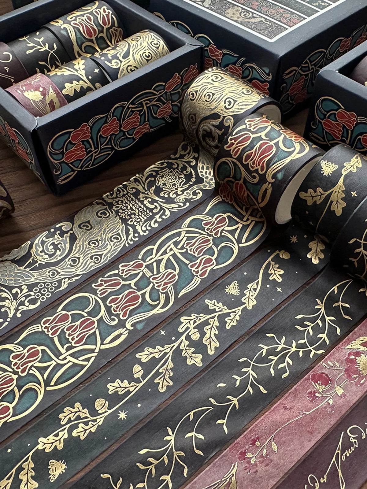 A set of metallic gold washi tape featuring floral and vine patterns on dark paper, displayed next to a wooden box.