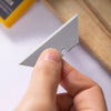 A hand holds a silver precision T-shape knife blade, showing its profile and edge.