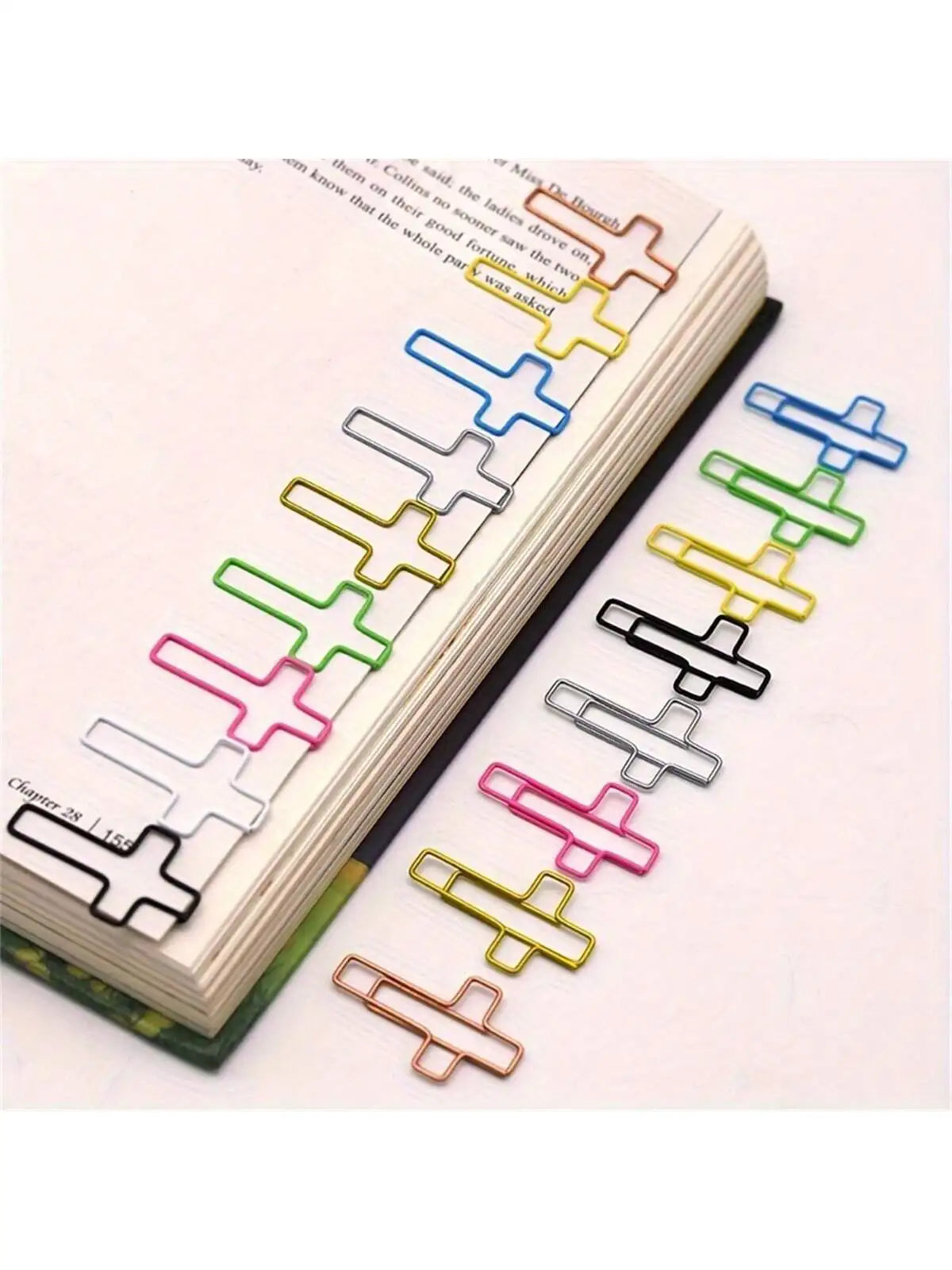 A set of cross-shaped metal paper clips in various colors, laid out next to a page of a notebook.