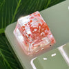 Translucent botanical resin keycaps with red floral inclusions resting on a green surface.