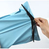 A hand is opening a light blue reusable waterproof poly shipping bag, showing the black sealing strip.