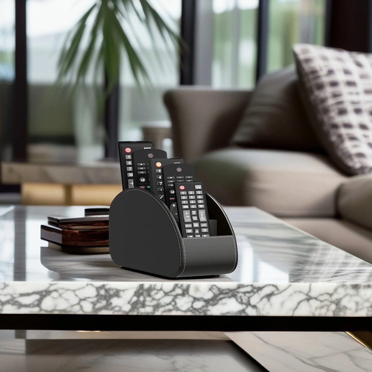 A black remote control holder and desk organizer tray with multiple remotes resting on a marble table in a modern living room