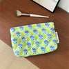 A light green floral quilted ladies clutch purse resting on a wooden surface next to a makeup brush.