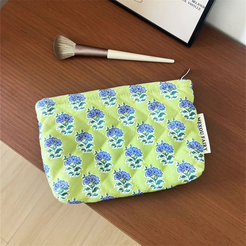 A light green floral quilted ladies clutch purse resting on a wooden surface next to a makeup brush.