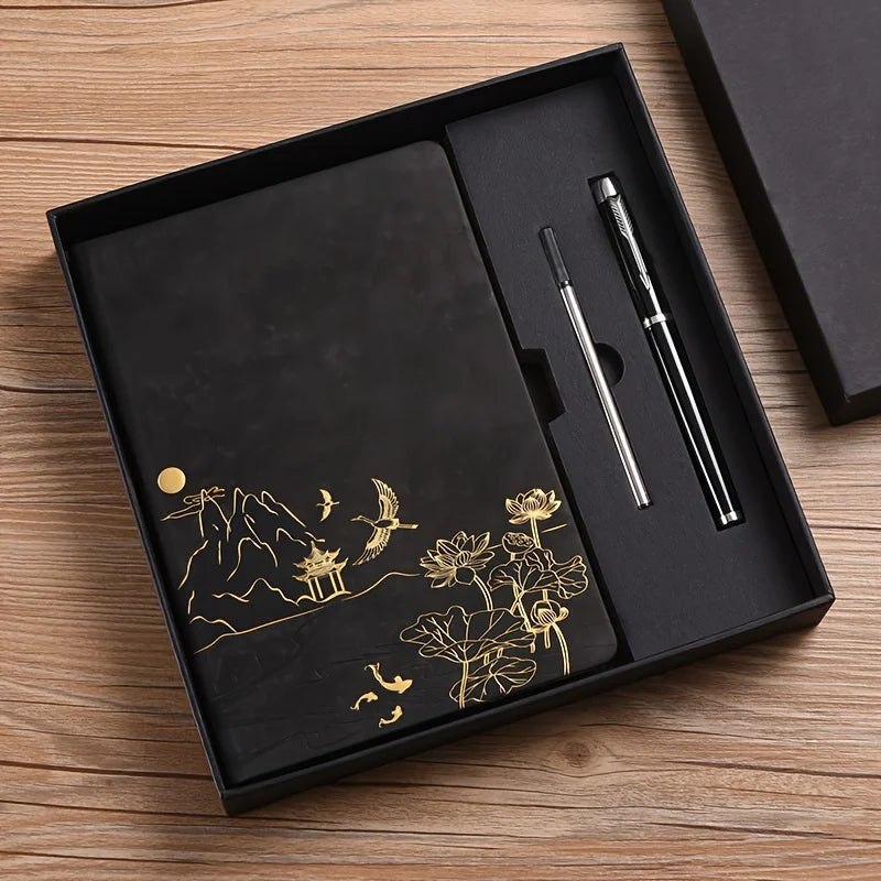 A black box containing a luxury notebook set with gold foil designs and two pens on a wooden surface.