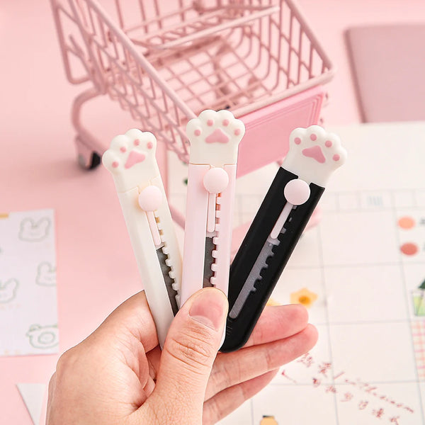 A hand holds three pink and black portable pet claw tools for crafting and decoration on a white surface.