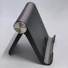A black foldable desktop phone holder with a silver circular opening and a metal clamp.