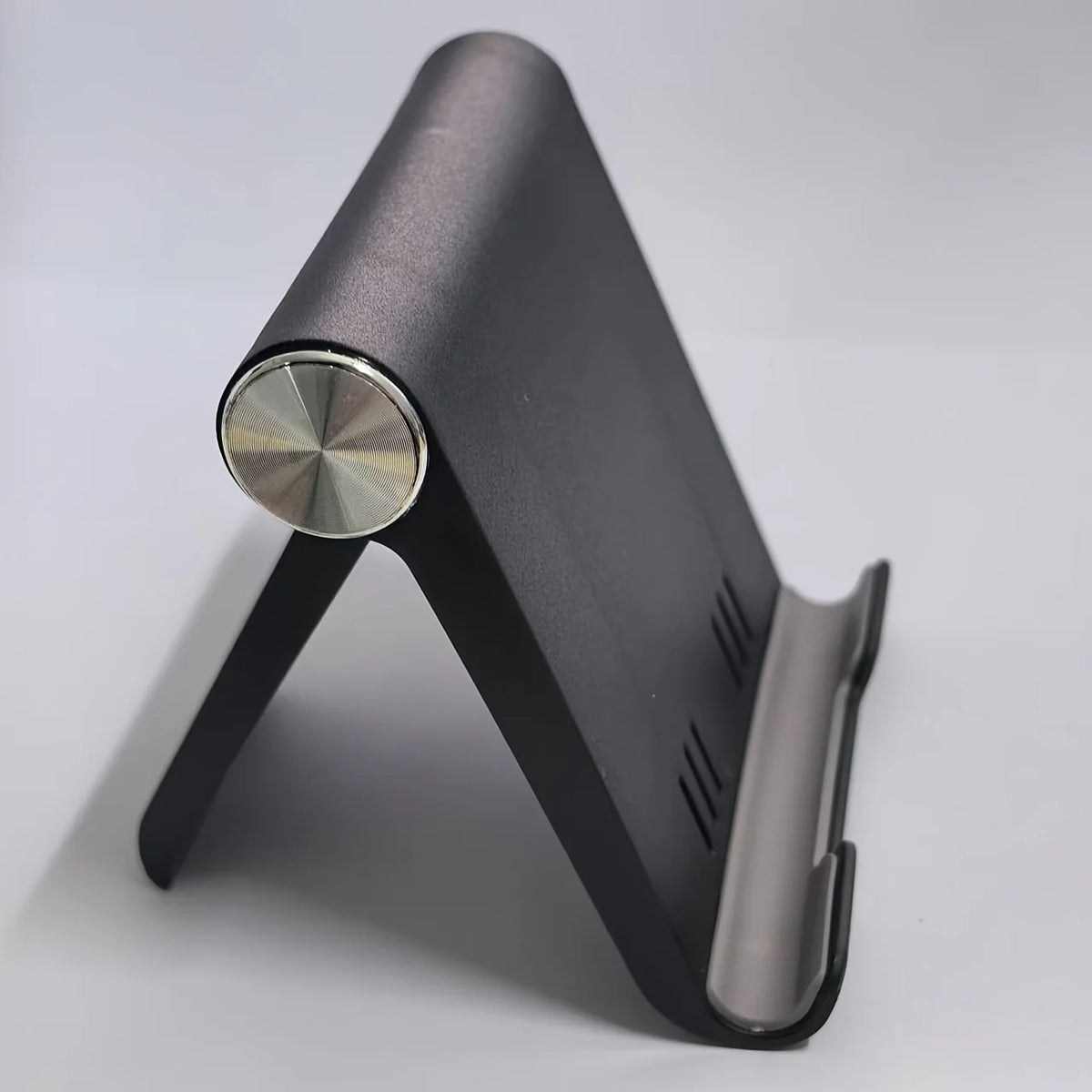 A black foldable desktop phone holder with a silver circular opening and a metal clamp.