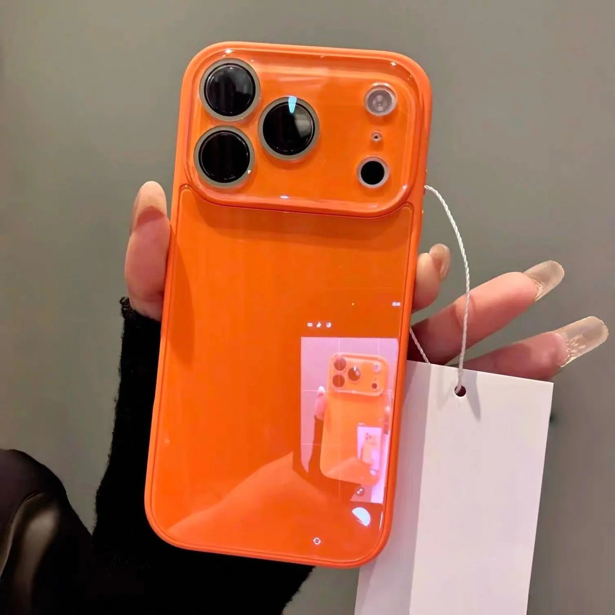 An orange iPhone in a glossy tempered glass shockproof case is held against a gray background.