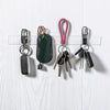 A collection of various keys and a dark green leather pouch hanging on a white wooden surface.