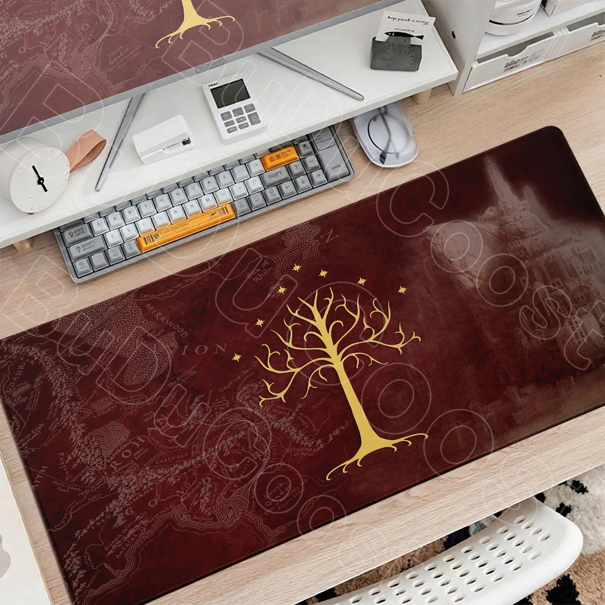 A large dark brown gaming mouse pad featuring a gold tree design placed on a wooden desk with computer accessories.