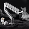 A silver adjustable desk monitor arm is shown extending over a dark surface with a small white figure and rocks.