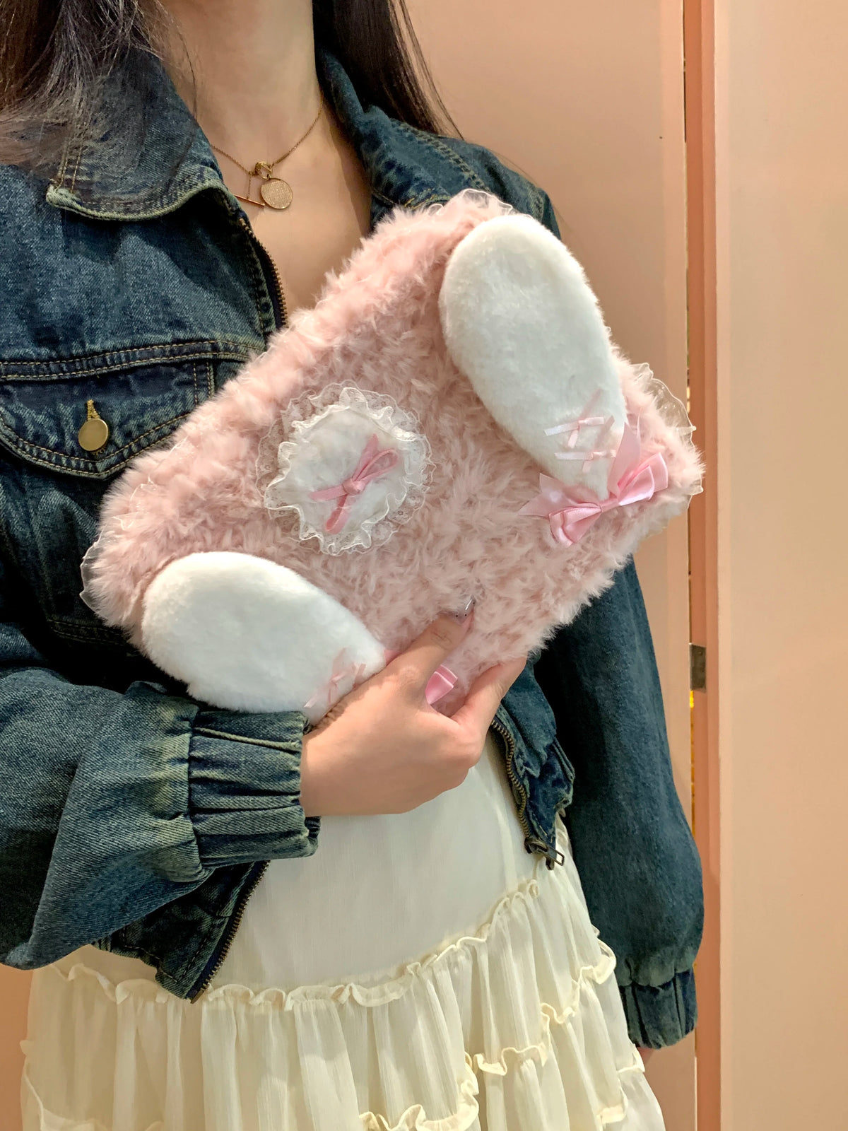 A person holds a pink fluffy rabbit plush case with white ears and pink accents.