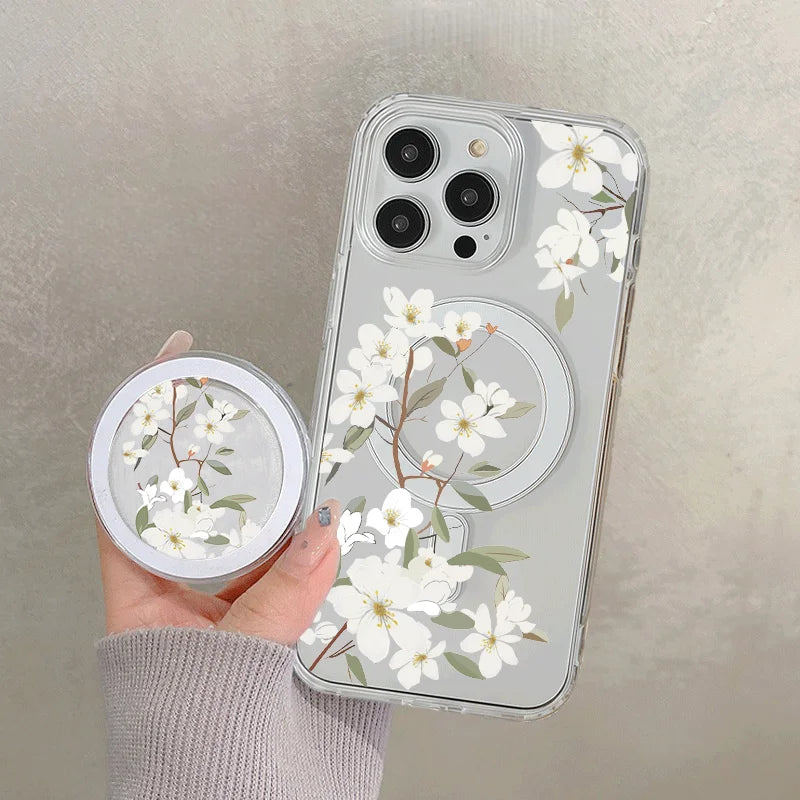 A hand holds a clear floral magnetic phone case for an iPhone featuring white blossoms and green leaves.