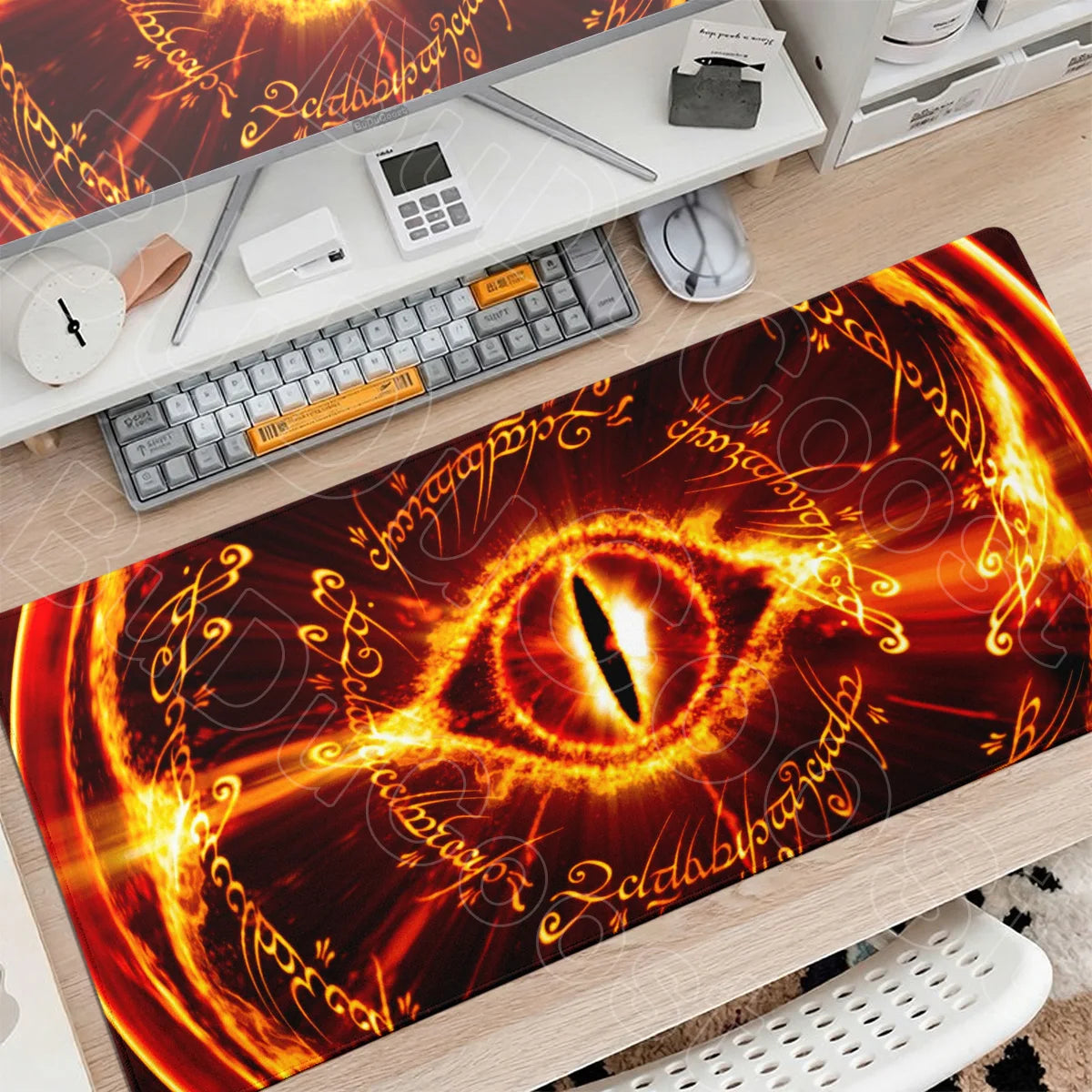 An orange and black Lord of the Rings themed gaming mouse pad placed on a wooden desk with a keyboard and mouse.