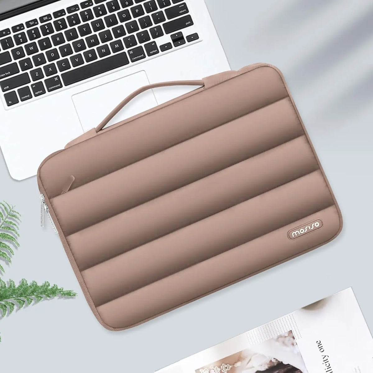 A tan protective laptop sleeve bag with reinforced padding resting on a light gray surface next to a laptop.