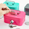 A hand opens a pink steel cash box with a key lock and removable tray, showing the inside.