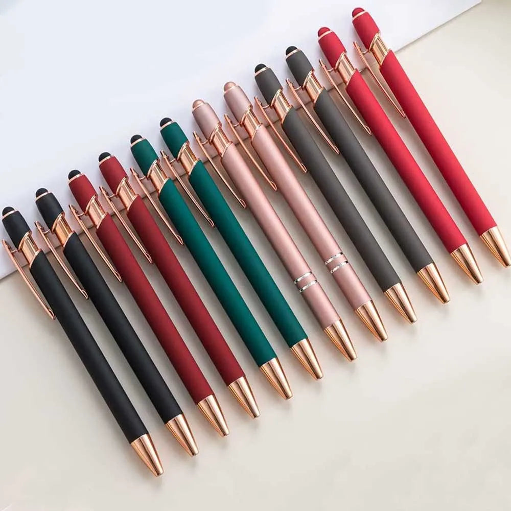 A collection of 12 retractable stylus and ballpoint pens in various shades of pink, red, and green are arranged on a white su