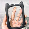 Eine Hand hält einen schwarzen Silikon-Katzen-Schlüsselanhänger mit Fingerabdruckmuster auf einer klaren Oberfläche.