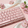 A close-up of a pink mechanical keyboard with light pink keycaps resting on a satin fabric background.