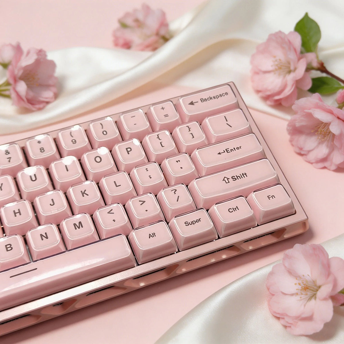 A close-up of a pink mechanical keyboard with light pink keycaps resting on a satin fabric background.