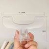 A hand holds a clear plastic book page clip designed to hold paper pages together.