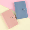A light pink reusable envelope binder with a blue cover and a matching pink folder lying on a pale yellow surface.
