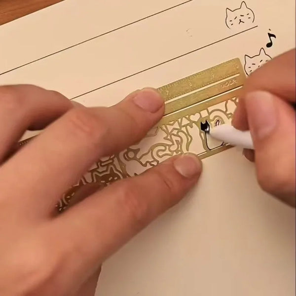 Hands are using a gold-colored metal bookmark ruler with a cat design to mark a page.