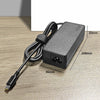 A black universal 65W USB-C laptop charger with a coiled cable is shown on a wooden surface.