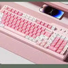 Eine rosa dreifache mechanische Tastatur auf einer hellrosa Oberfläche neben einem Smartphone.