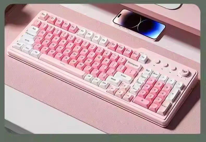 Eine rosa dreifache mechanische Tastatur auf einer hellrosa Oberfläche neben einem Smartphone.