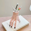 A pink resin palm hand decoration with black spots holds several white and green paintbrushes.