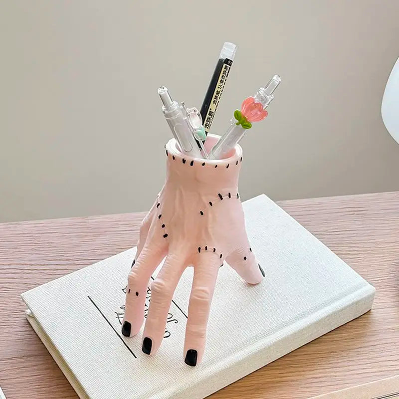 A pink resin palm hand decoration with black spots holds several white and green paintbrushes.