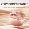 A pink open ear clip Bluetooth earbud charging case is shown resting on a sandy background.