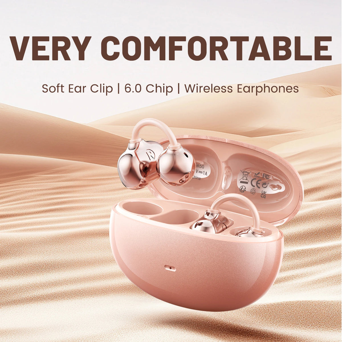 A pink open ear clip Bluetooth earbud charging case is shown resting on a sandy background.
