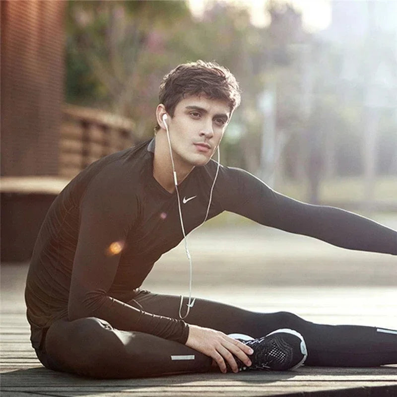A young man wearing a black long-sleeved shirt is lying down outdoors with wired Type-C earphones connected to his ear.