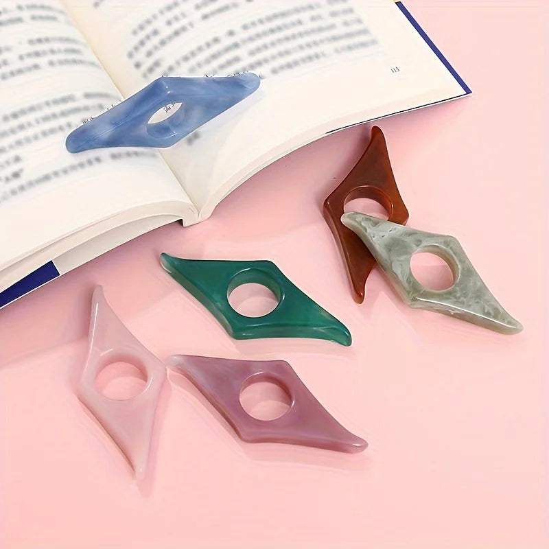 A collection of resin thumb book stands in various shades of blue, green, pink, and brown resting on an open book.