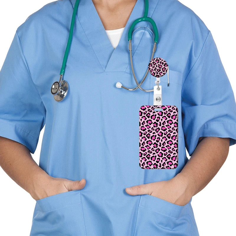 A person wearing light blue scrubs holds a leopard print retractable badge holder with a stethoscope attached.