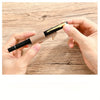 A hand holds a black pen with a leather holder and gold keychain on a wooden surface.
