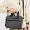 A gray Oxford cloth crossbody briefcase with a laptop compartment is shown being held by a person.