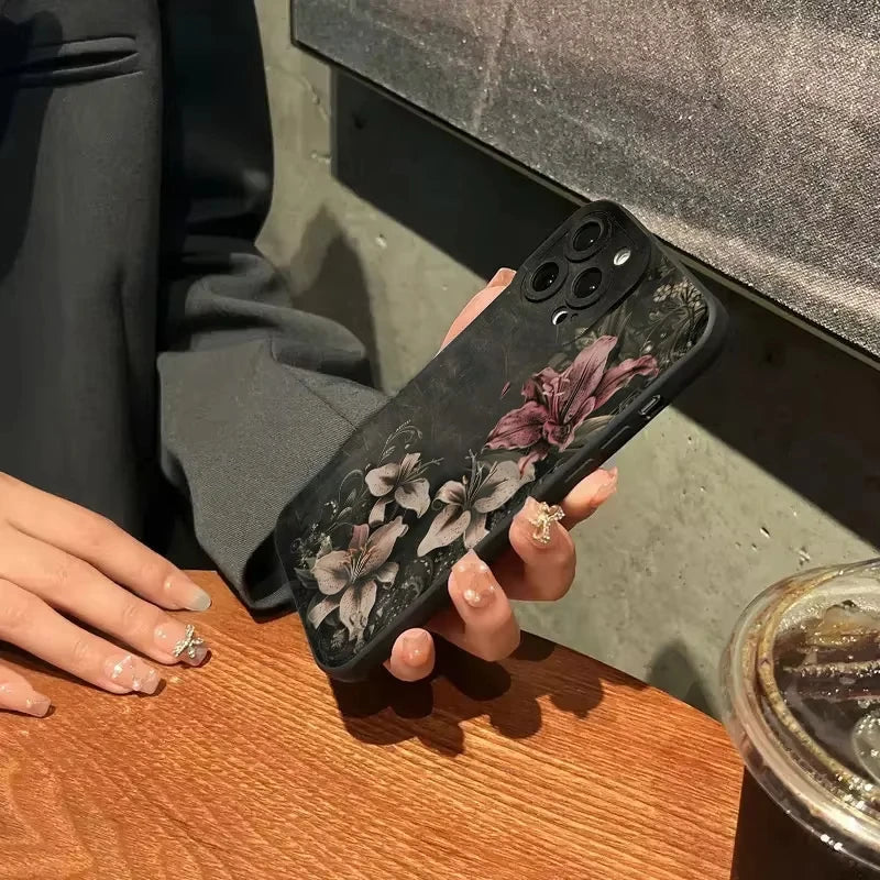A hand holds a black phone case featuring gothic floral art on a wooden surface.