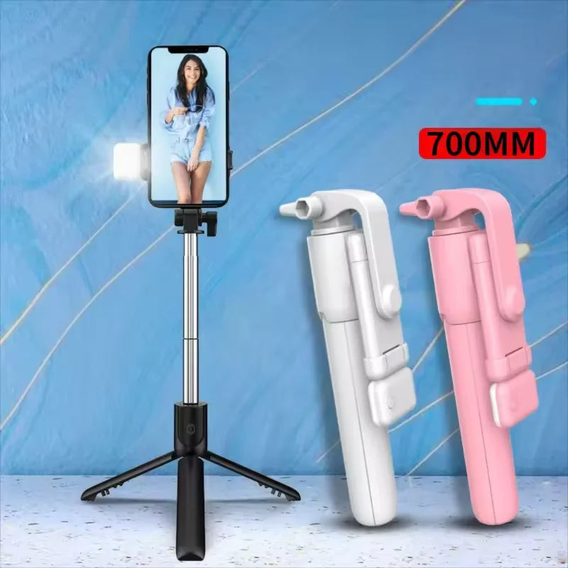 A white selfie stick tripod with a fill light and wireless remote is shown next to two pink and white camera grips.