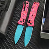 A pair of pink acrylic folding knives with colorful inserts and D2 steel blades resting on a dark surface.
