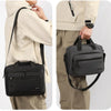 A man wearing a beige jacket holds a black Oxford cloth crossbody briefcase with a laptop compartment.