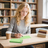 Eine junge Frau schreibt auf grünen Indexkarten an einem Holzschreibtisch in einer Bibliothek.