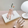 A hand decoration made of pink resin palm with black details and several thin white sticks.