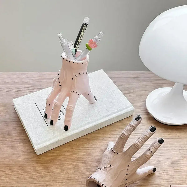A hand decoration made of pink resin palm with black details and several thin white sticks.