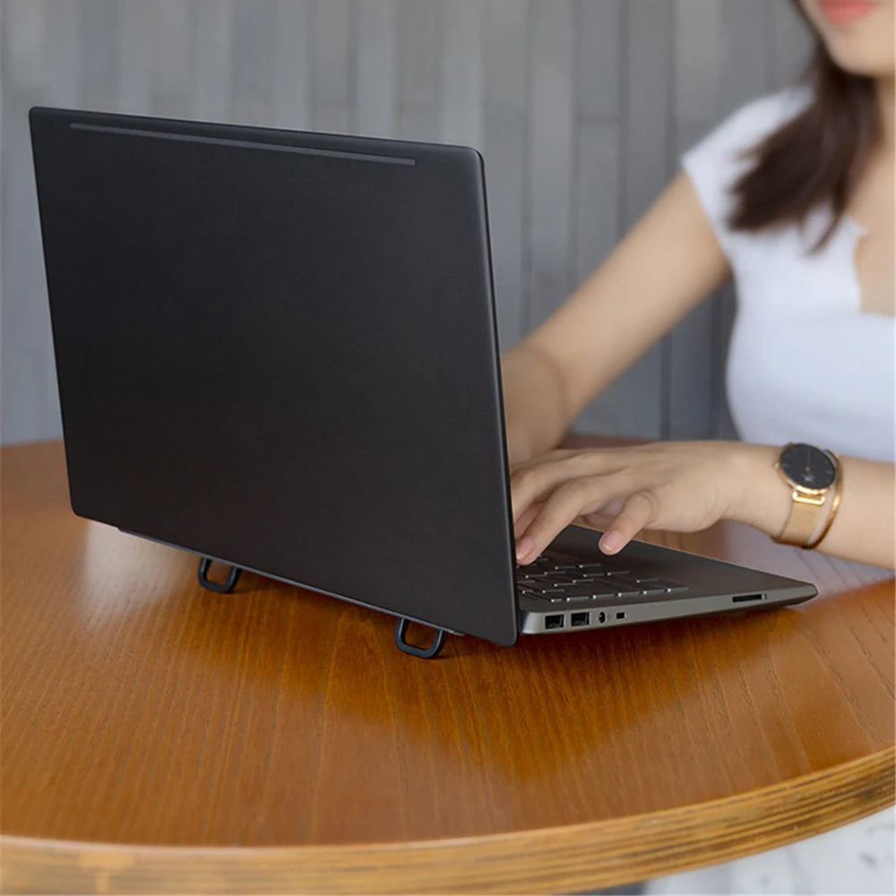 Una persona está usando un soporte portátil de laptop de aluminio negro en un escritorio de madera.