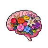 An enamel pin shaped like a pink brain filled with colorful flowers and leaves.